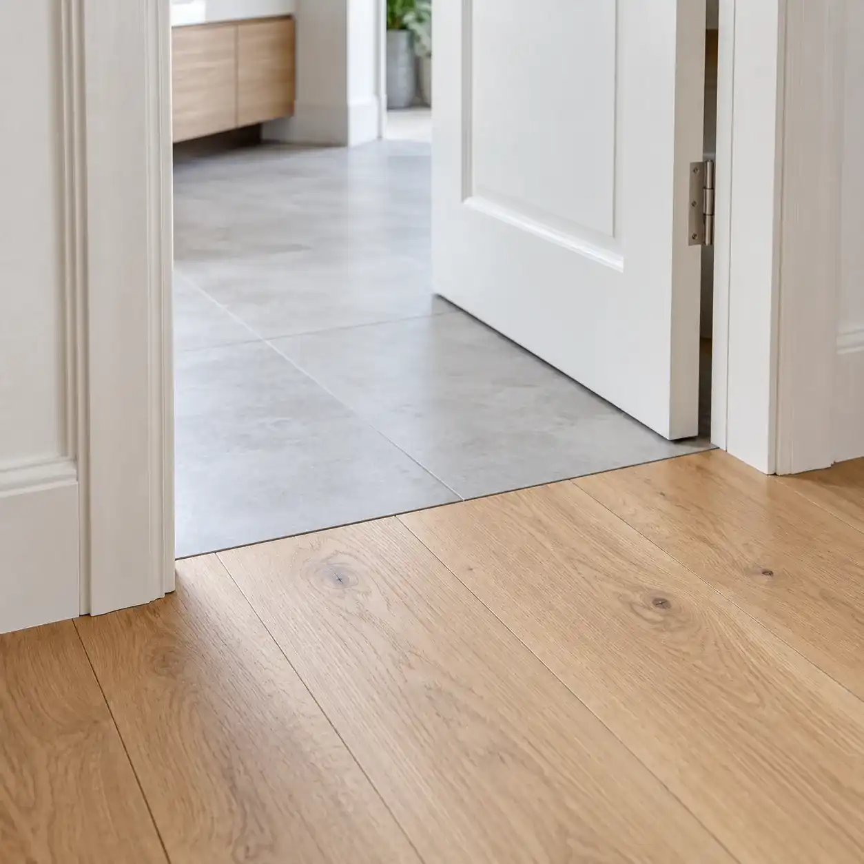 Parquet chêne clair et carrelage gris qui se rejoignent sous une porte