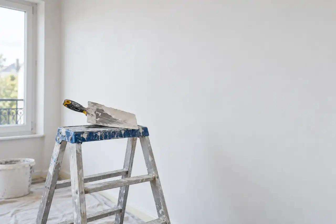Mur parfaitement lisse à l'enduit blanc, couteau posé sur un escabeau